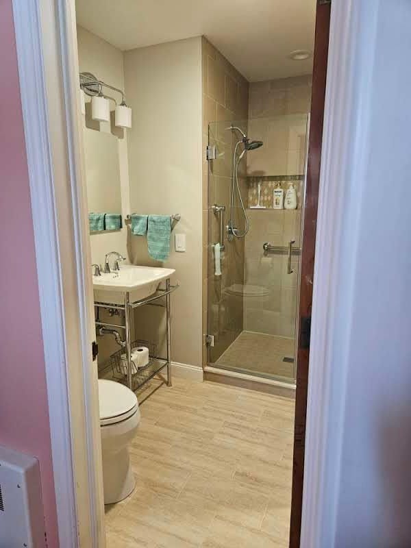 bathroom with toilet, an enclosed shower, sink, and hardwood / wood-style floors