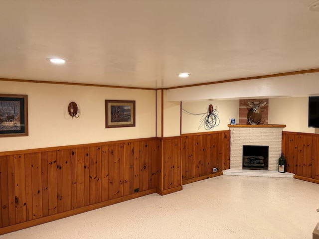 basement featuring wood walls, crown molding, and a brick fireplace