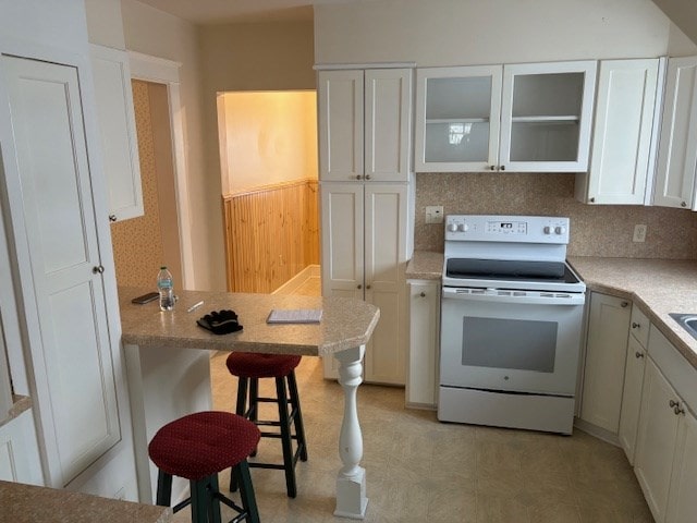 kitchen with kitchen peninsula, decorative backsplash, a kitchen bar, white range with electric stovetop, and white cabinets