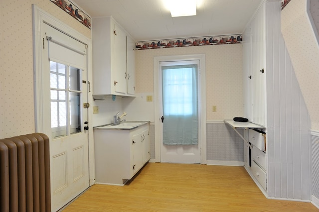 kitchen with radiator heating unit, light hardwood / wood-style flooring, and white cabinets