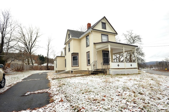 snow covered rear of property featuring covered porch