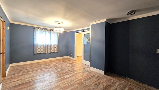 spare room with wood-type flooring, ornamental molding, and a barn door