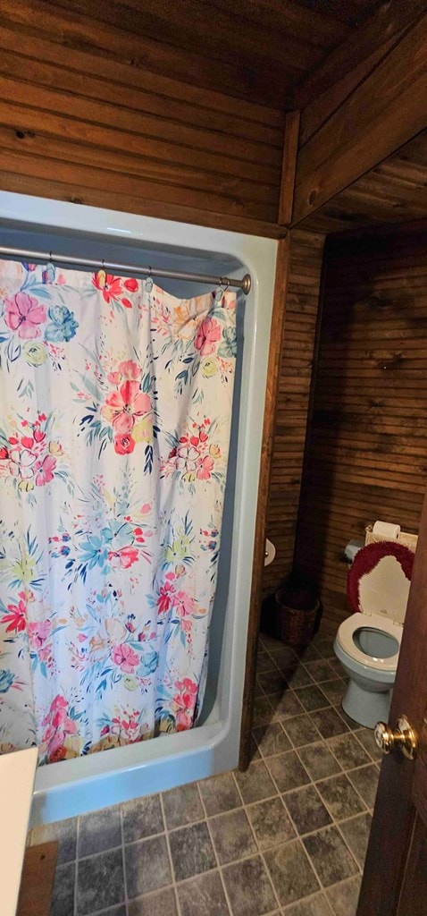 bathroom with wooden walls, toilet, and a shower with curtain