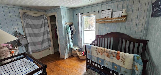 bedroom with wooden walls, a crib, and hardwood / wood-style flooring