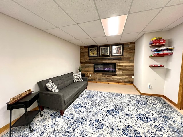 carpeted living room with a drop ceiling, wooden walls, and a fireplace