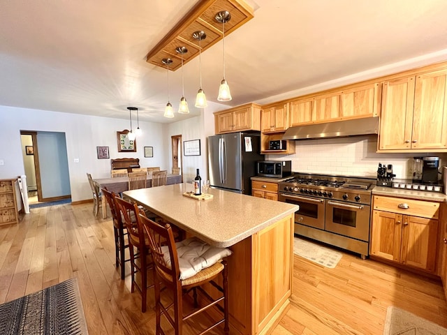 kitchen featuring tasteful backsplash, hanging light fixtures, light hardwood / wood-style flooring, appliances with stainless steel finishes, and a kitchen island