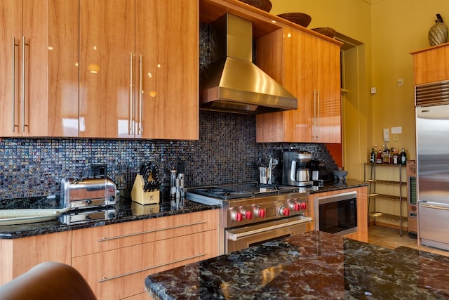 kitchen with tasteful backsplash, dark stone countertops, range hood, built in appliances, and light tile patterned floors