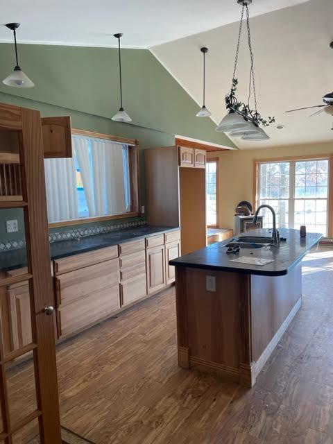 kitchen with lofted ceiling, dark hardwood / wood-style floors, a center island with sink, sink, and hanging light fixtures