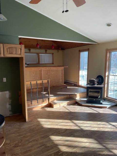 kitchen featuring ceiling fan, a wood stove, wood-type flooring, and lofted ceiling