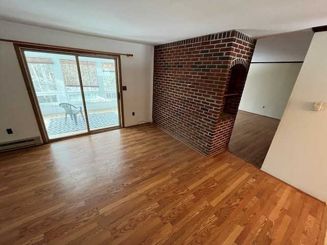 empty room featuring hardwood / wood-style flooring, brick wall, and baseboard heating