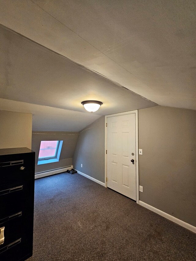 additional living space featuring vaulted ceiling, dark carpet, and baseboard heating