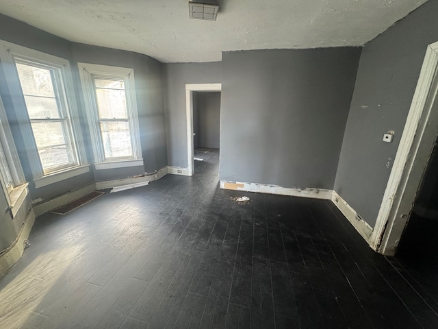 unfurnished room featuring dark wood-type flooring, plenty of natural light, and a textured ceiling