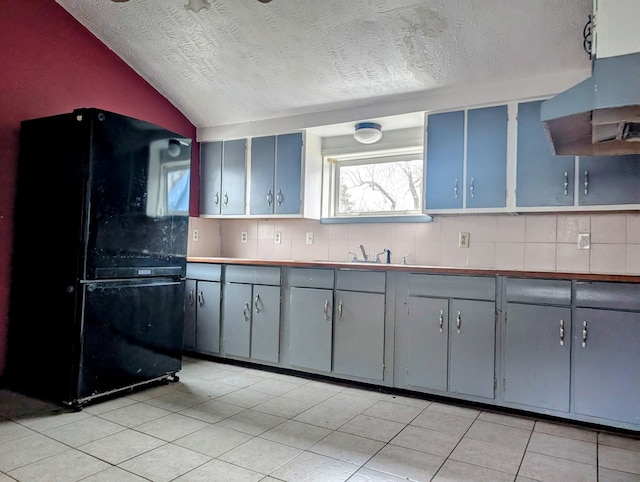 kitchen with gray cabinets, black refrigerator, ventilation hood, and vaulted ceiling