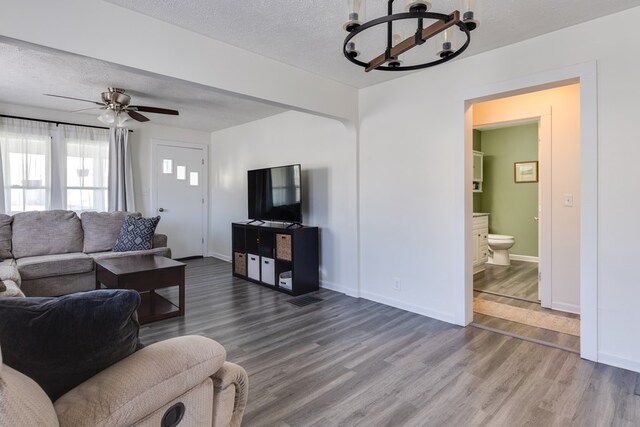 living room featuring wood-type flooring, ceiling fan with notable chandelier, and a textured ceiling