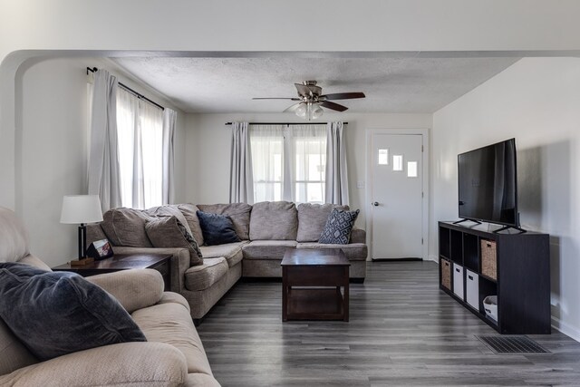 living room with dark hardwood / wood-style flooring, ceiling fan, and a textured ceiling