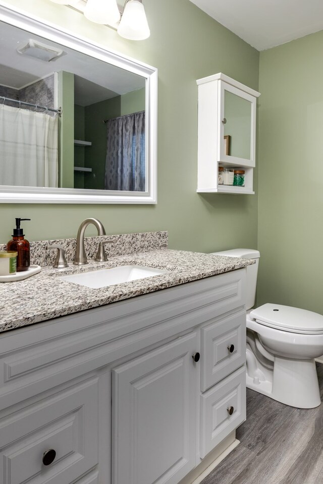 bathroom featuring wood-type flooring, toilet, a shower with shower curtain, and vanity