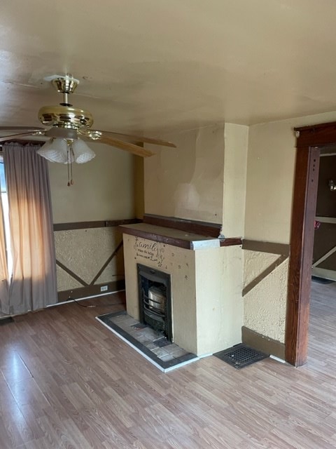 unfurnished living room featuring hardwood / wood-style flooring, ceiling fan, and a wood stove