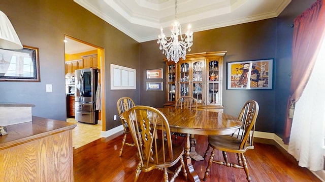 dining space with crown molding, hardwood / wood-style floors, a notable chandelier, and a tray ceiling