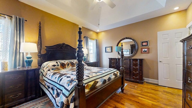 bedroom with a raised ceiling, light wood-type flooring, and ceiling fan