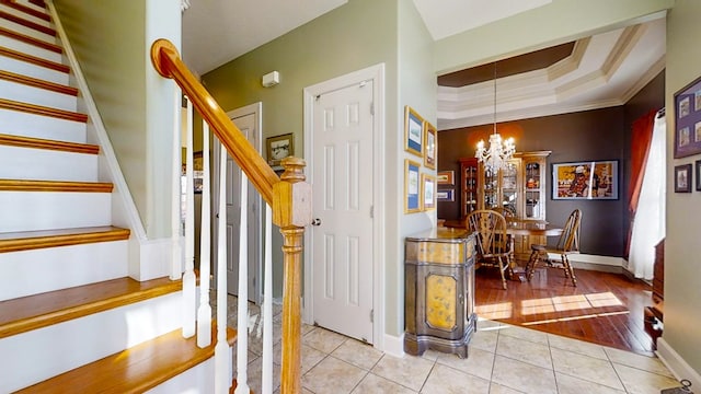 stairway with a notable chandelier, crown molding, tile patterned floors, and a tray ceiling