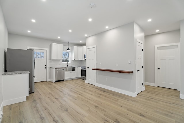 kitchen with sink, appliances with stainless steel finishes, white cabinetry, hanging light fixtures, and tasteful backsplash