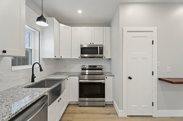 kitchen with pendant lighting, appliances with stainless steel finishes, tasteful backsplash, light hardwood / wood-style floors, and white cabinets