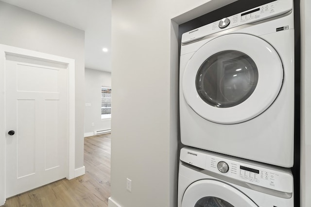 clothes washing area featuring stacked washing maching and dryer, baseboard heating, and light hardwood / wood-style flooring