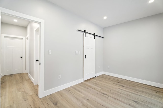 unfurnished room with a barn door and light hardwood / wood-style floors