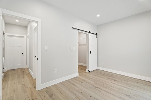 unfurnished bedroom with a barn door and light hardwood / wood-style flooring