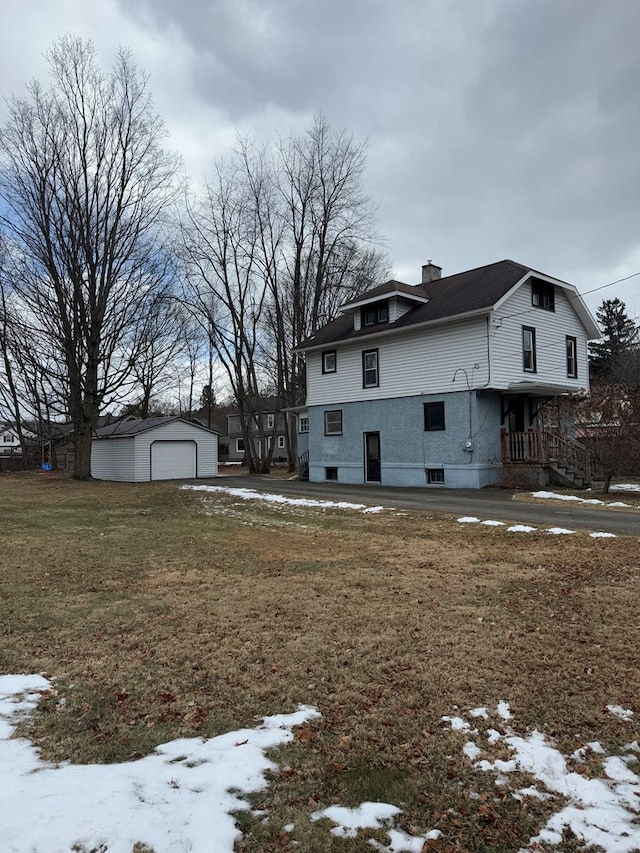 view of snowy exterior featuring a garage, an outdoor structure, and a yard