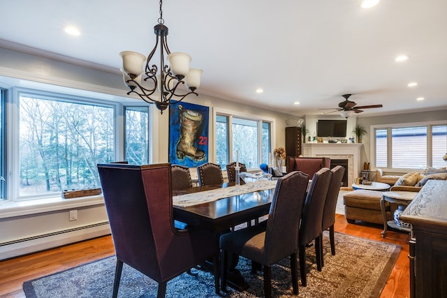 dining room featuring baseboard heating, ornamental molding, wood-type flooring, and ceiling fan with notable chandelier