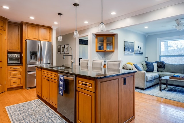 kitchen with appliances with stainless steel finishes, pendant lighting, sink, a center island with sink, and light wood-type flooring