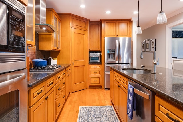 kitchen with wall chimney range hood, appliances with stainless steel finishes, hanging light fixtures, dark stone counters, and light wood-type flooring