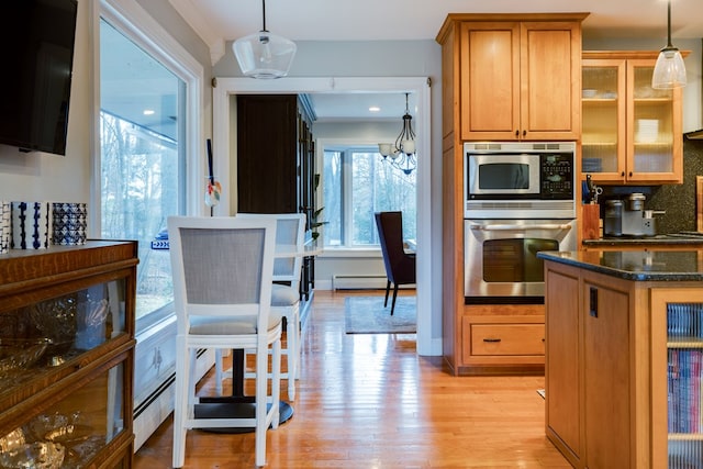 kitchen with pendant lighting, light hardwood / wood-style flooring, baseboard heating, appliances with stainless steel finishes, and dark stone counters