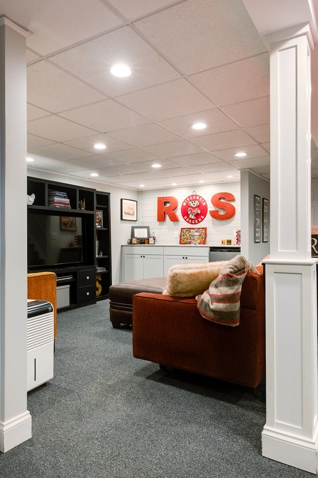 carpeted living room with a drop ceiling, built in shelves, and ornate columns