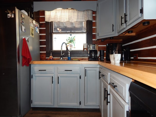 kitchen with dishwashing machine, sink, butcher block countertops, stainless steel refrigerator, and white cabinets