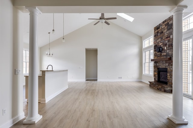 unfurnished living room featuring ceiling fan, high vaulted ceiling, a stone fireplace, and decorative columns