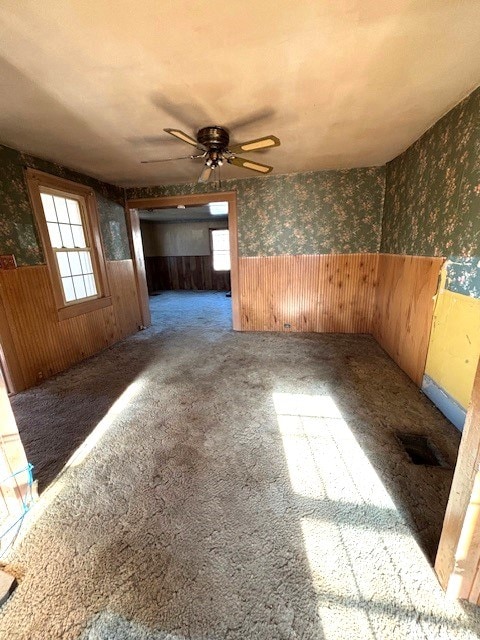 unfurnished room with carpet floors, wooden walls, and ceiling fan