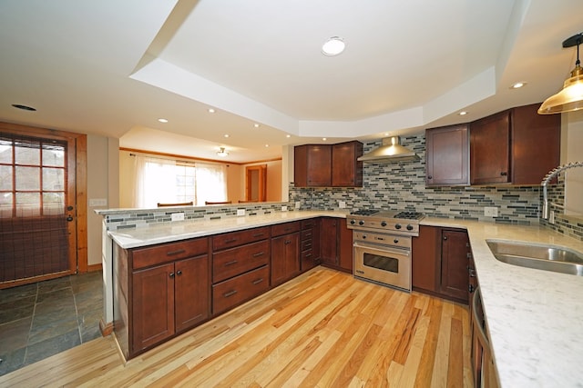 kitchen featuring pendant lighting, sink, wall chimney range hood, appliances with stainless steel finishes, and kitchen peninsula