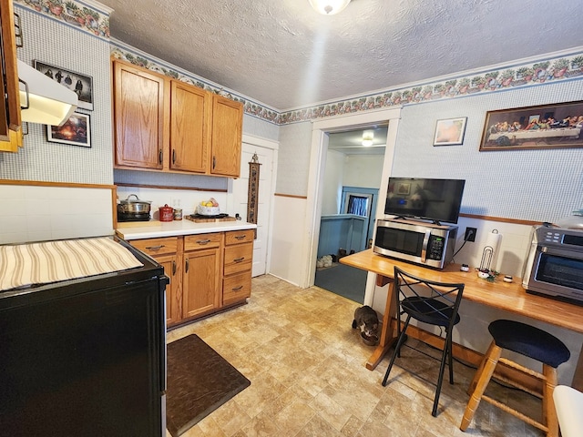 kitchen with black electric range oven, a textured ceiling, and built in desk