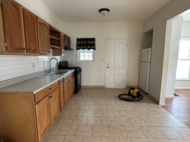 kitchen featuring black electric range oven, sink, white refrigerator, a healthy amount of sunlight, and decorative backsplash