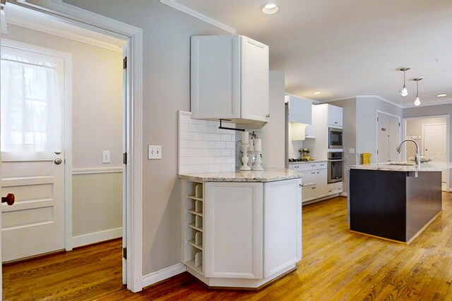 kitchen with white cabinets, backsplash, hanging light fixtures, stainless steel appliances, and light hardwood / wood-style flooring