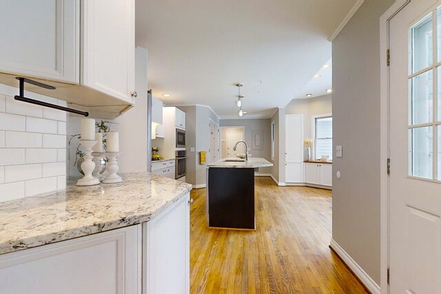 kitchen with tasteful backsplash, white cabinetry, sink, oven, and light stone countertops