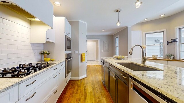 kitchen featuring appliances with stainless steel finishes, sink, white cabinets, hanging light fixtures, and light stone countertops