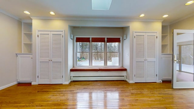 unfurnished bedroom with a baseboard heating unit, ornamental molding, multiple closets, and light wood-type flooring