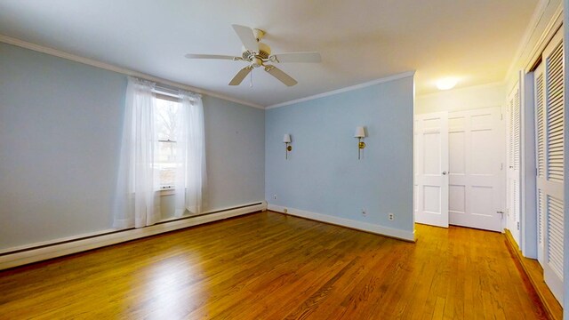 interior space with a baseboard radiator, wood-type flooring, ornamental molding, ceiling fan, and a closet