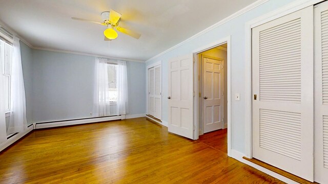 unfurnished bedroom featuring baseboard heating, crown molding, and hardwood / wood-style flooring