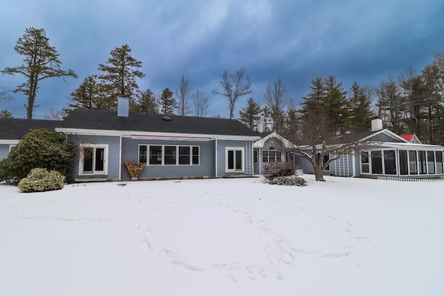 snow covered back of property with a sunroom