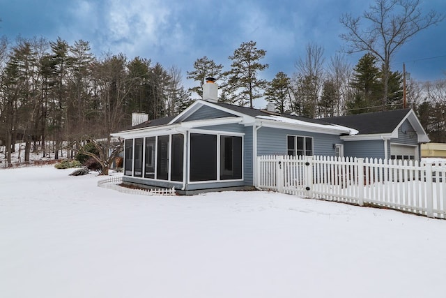 snow covered rear of property featuring a sunroom