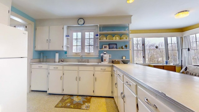 kitchen with white refrigerator, white cabinetry, and sink